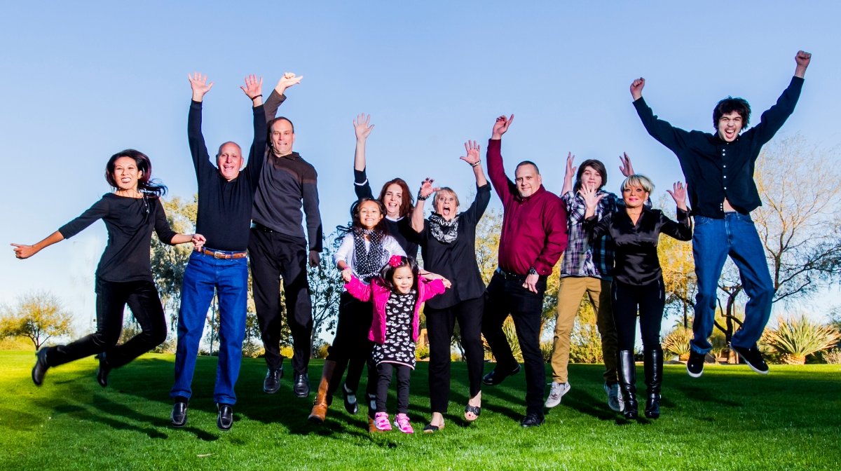 Family and friends jumping with smiles on a grassy field on a sunny day.