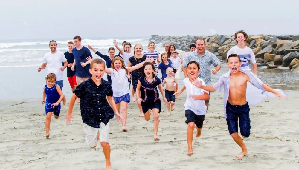 Group of children and adults running on a beach, smiling and enjoying a sunny day