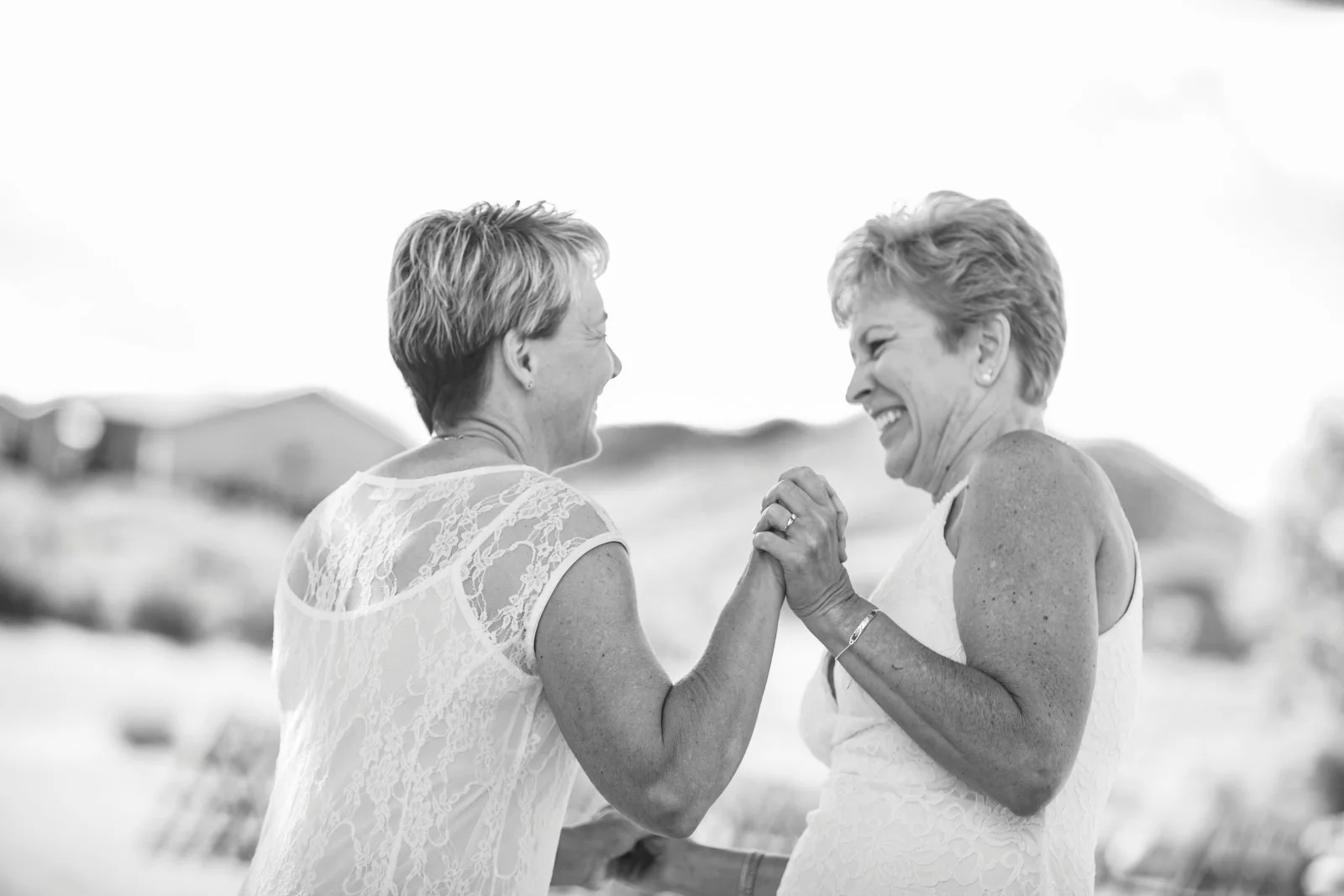 Two middle-aged women smiling and holding hands in a joyful moment outdoors