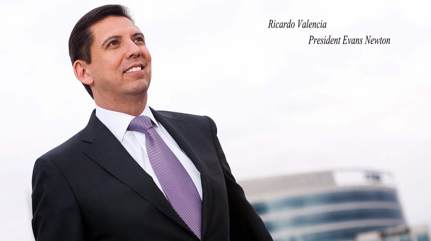 A man in a suit with a purple striped tie standing outdoors with a modern building in the background.