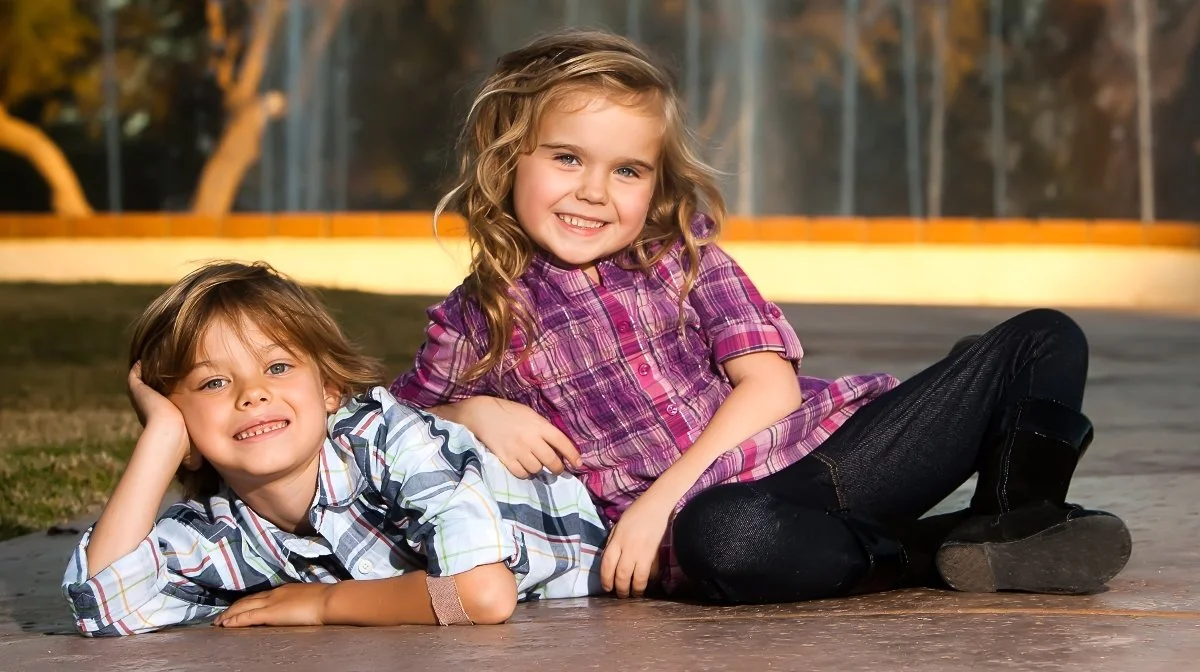 Two children, a boy and a girl, lying on the outdoor pavement, smiling and relaxing.