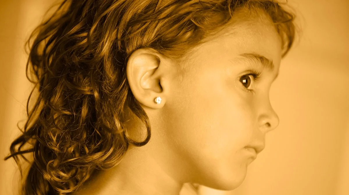 Close-up side profile of a young girl with curly hair and stud earrings.