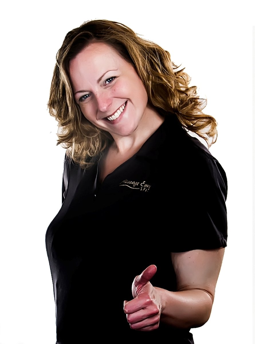 A woman with curly brown hair smiling and giving a thumbs-up gesture, wearing a black shirt with white text.