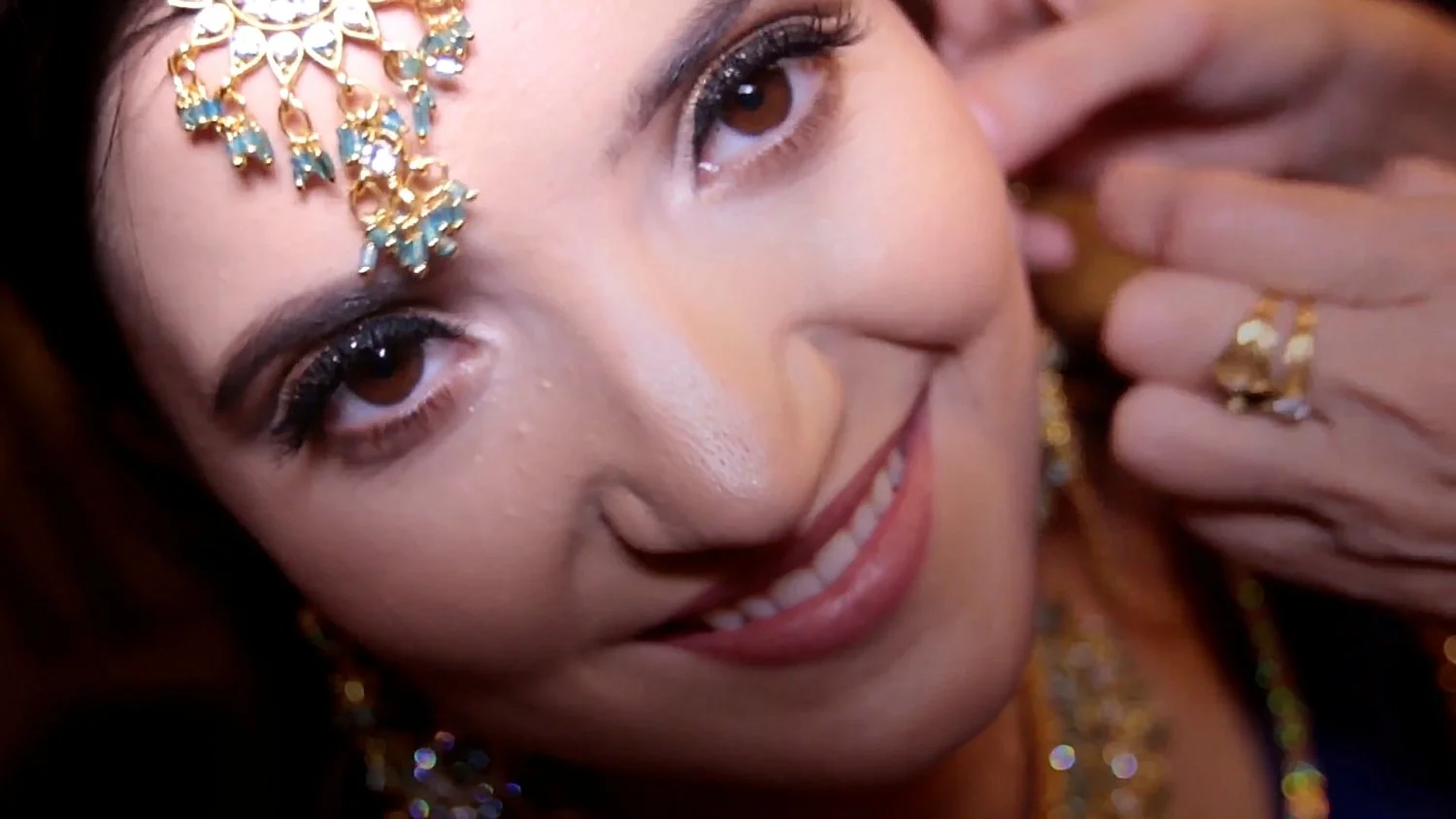 Close-up of a smiling woman with makeup, wearing gold jewelry and an ornate headpiece.