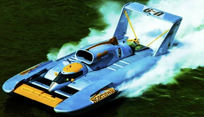 A blue speedboat racing on water, creating a large wake with water splashing behind it.
