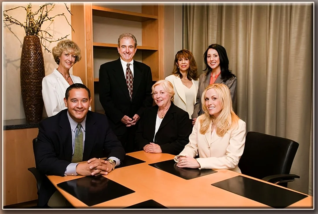 Group of seven professionally dressed people in a conference room, posing for a photo around a table.
