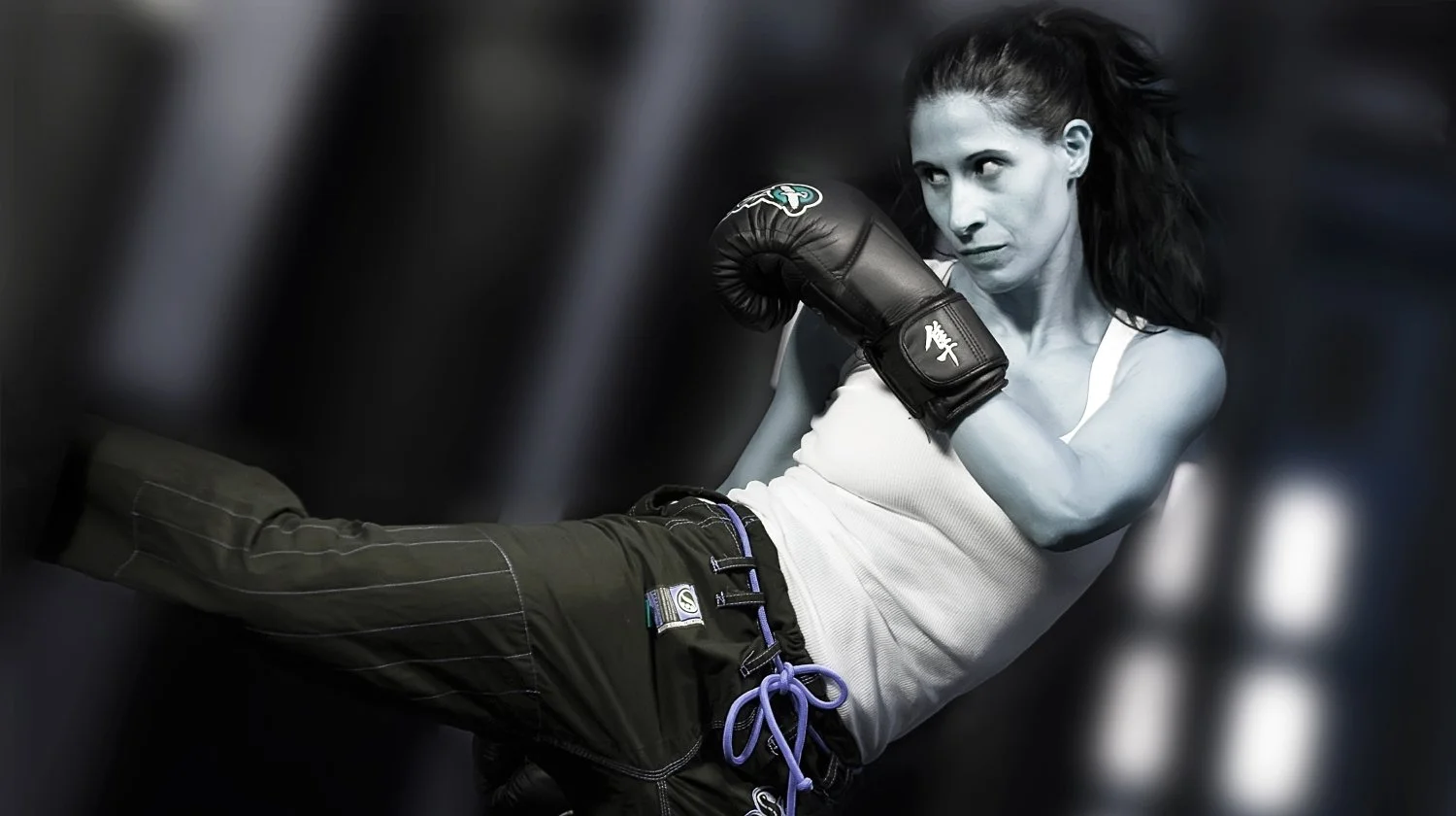 Black and white photo of a woman in a white tank top and military green shorts practicing boxing in a gym