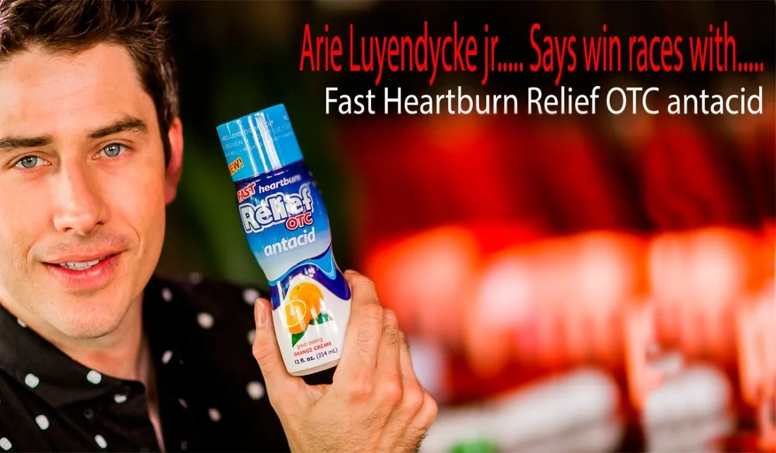 Man smiling and holding a bottle of Fast Heartburn Relief OTC antacid in front of a blurred background of other antacid bottles