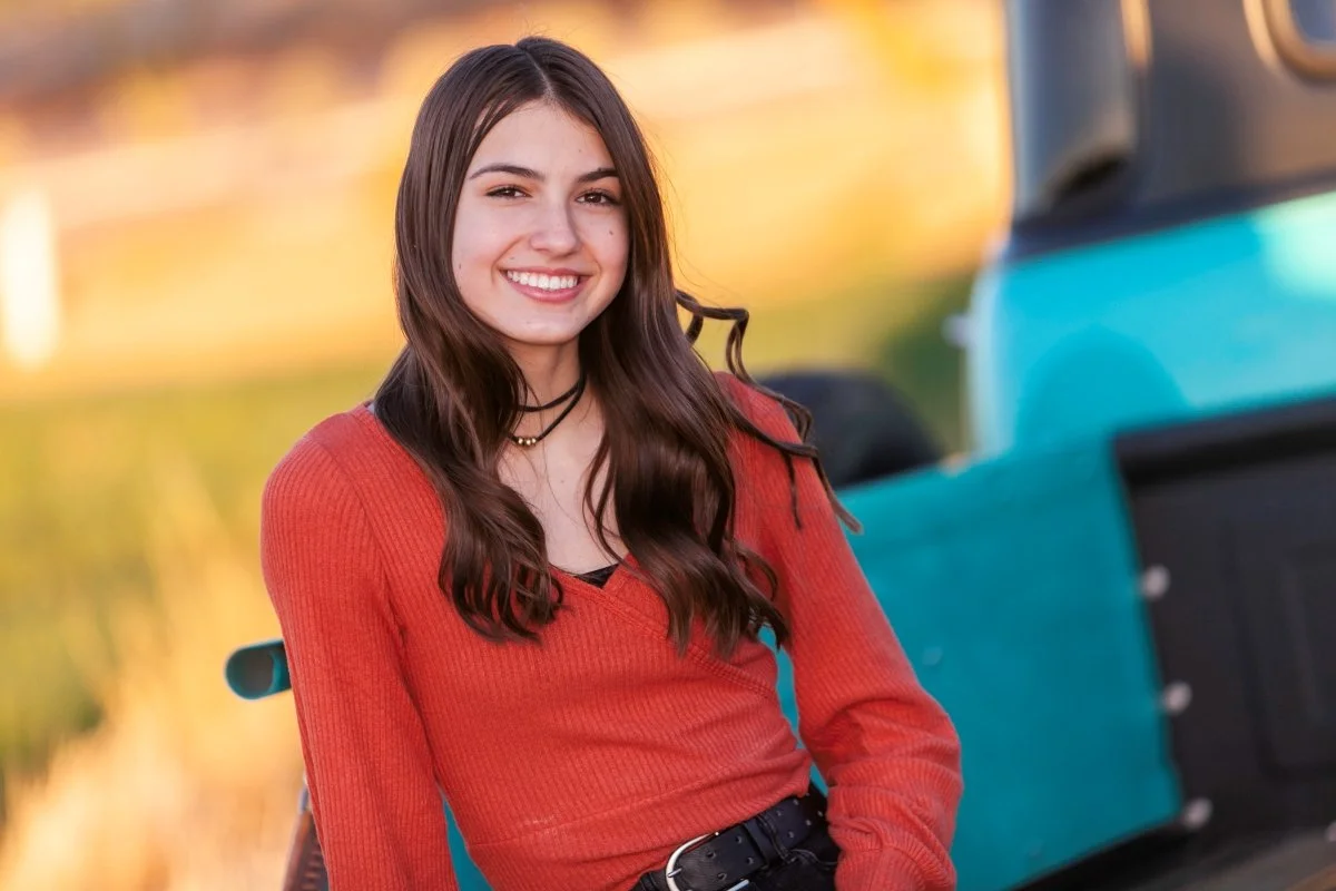 A young woman with long brown hair smiling outdoors near a blue vintage truck.