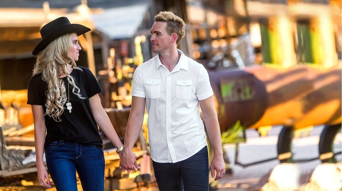 A young couple holding hands and looking at each other outdoors near vintage industrial equipment.