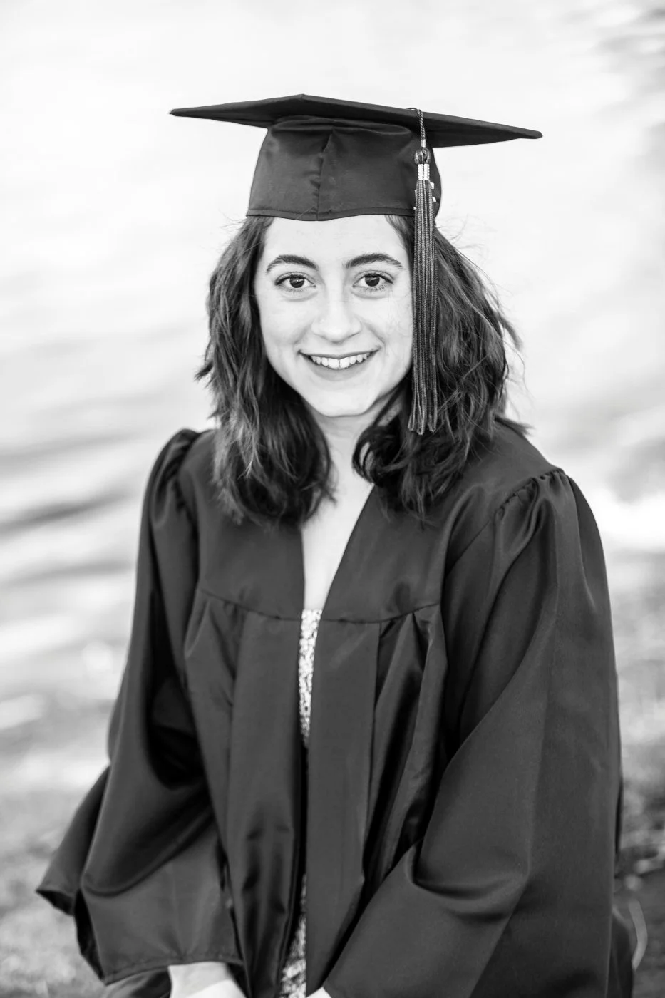 A young woman in graduation attire, wearing a cap and gown, smiling at the camera.
