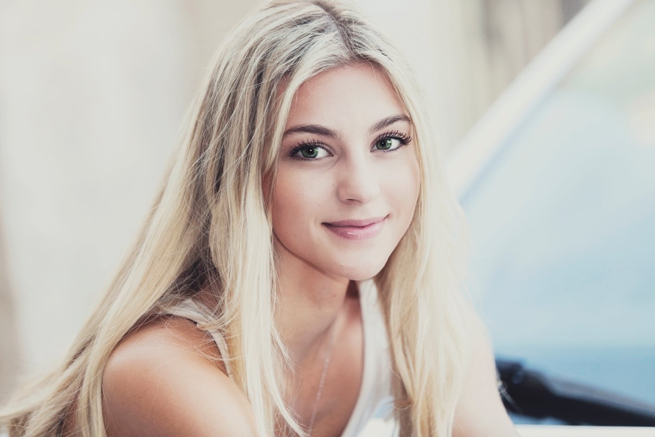 Close-up portrait of a young woman with long blonde hair and green eyes smiling at the camera.
