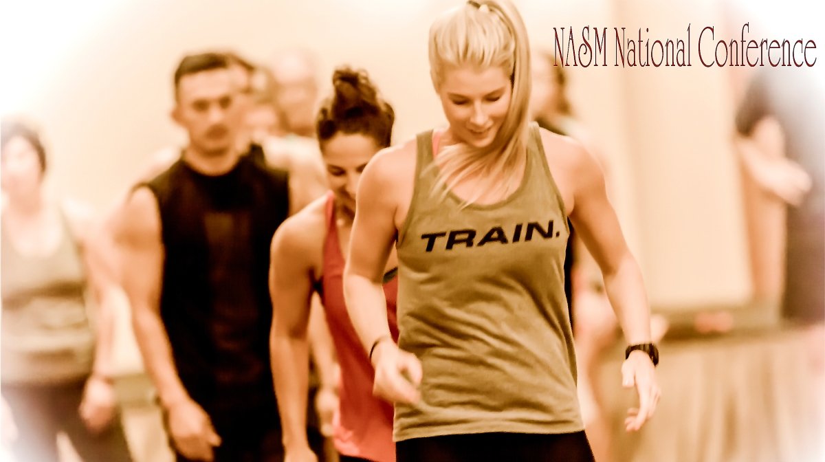 Group of athletes, mostly women, running indoors at NASM National Conference, with the woman in front wearing a tan tank top with 'TRAIN.' printed on it.