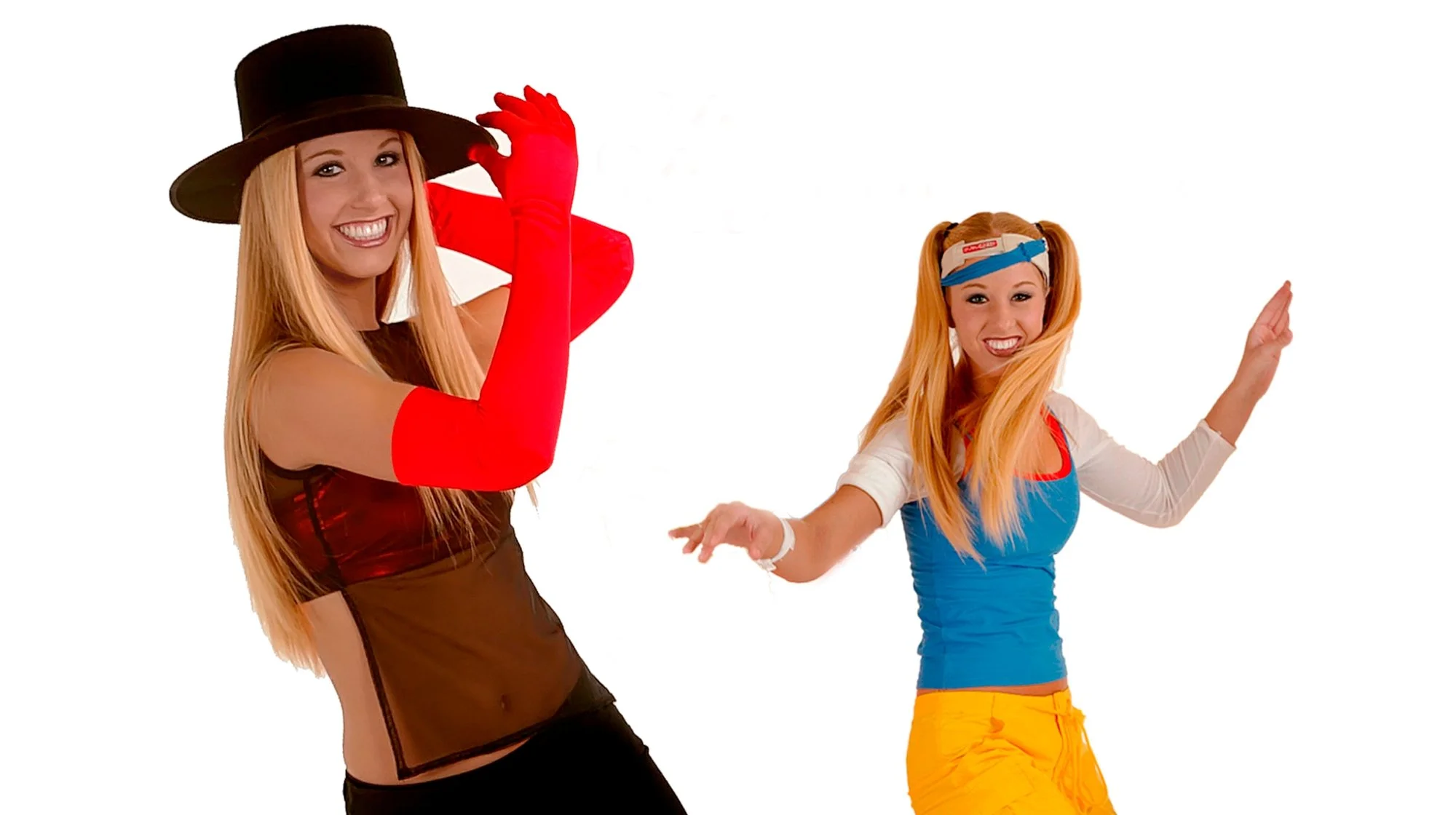 Two women dancing and smiling, dressed in colorful costumes, with one wearing a witch hat and red gloves, and the other wearing a headband and bright clothes, against a white background.