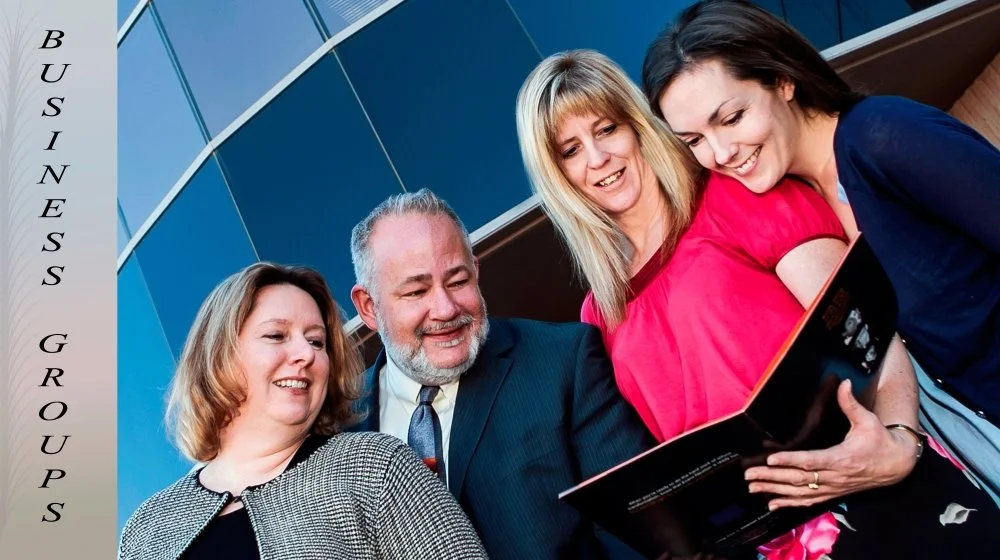 Four business people looking at a tablet outside a modern building, smiling and discussing.