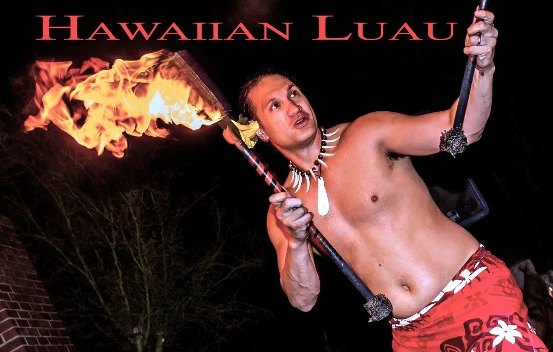 A man with a shirtless torso, wearing a Hawaiian-style skirt and a shell necklace, is holding two flaming fire poi, typical in Hawaiian luau performances, with open expressions of excitement or concentration.