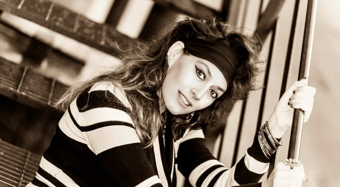 A young woman with curly hair, wearing a headband and striped shirt, holding onto a rail on an escalator.