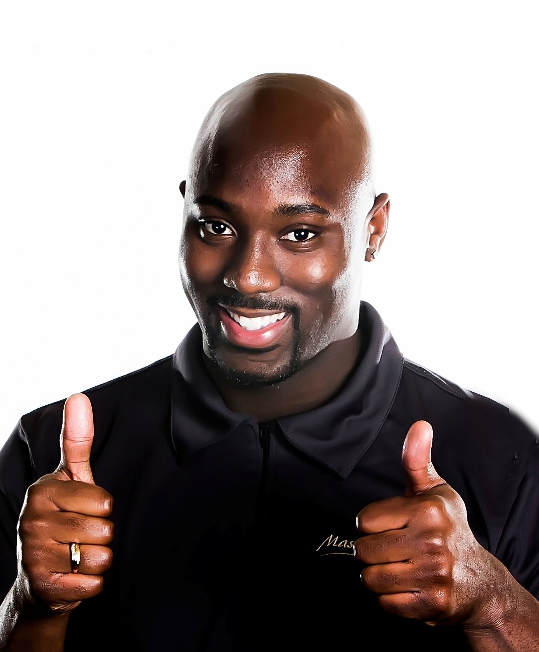 A smiling man with dark skin, a bald head, and a stubble beard, wearing a black shirt, giving two thumbs up.