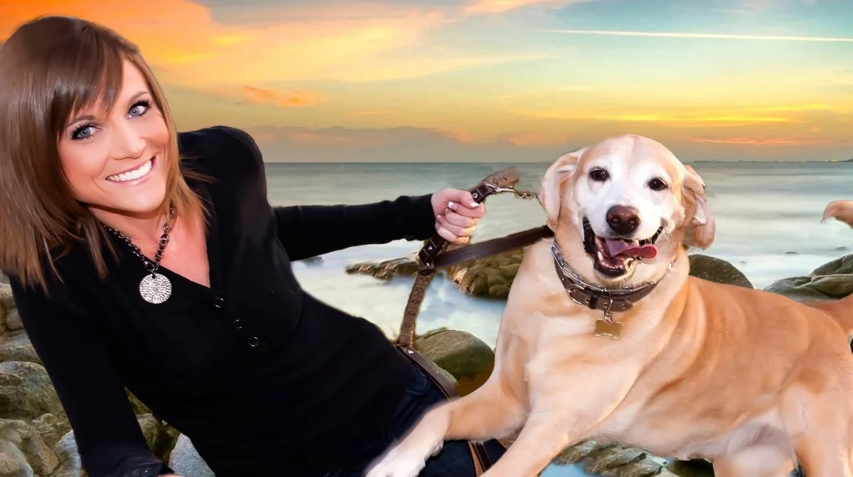 A woman in black with a necklace smiling while holding a leash attached to a happy yellow Labrador Retriever on the beach at sunset.