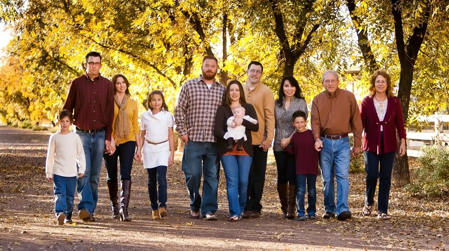 Family walking outdoors during fall, five adults and five children, with yellow autumn leaves in the background.