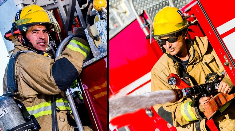 Two firefighters in protective gear and yellow helmets actively fighting a fire with hoses on a fire truck.