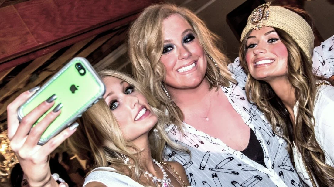 Three women taking a selfie together, smiling, at a social gathering.