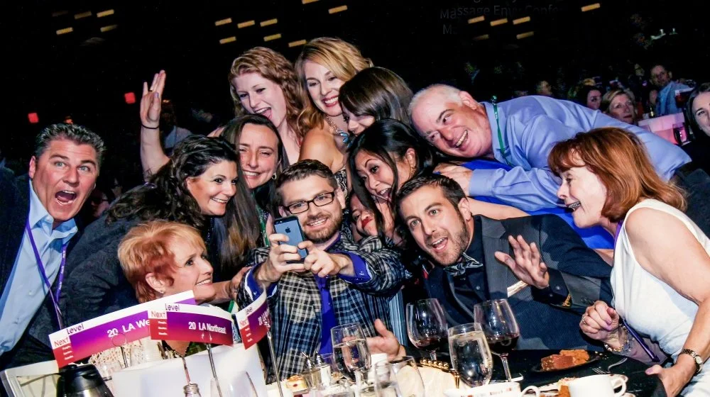 Group of people at a celebratory event, taking a selfie, smiling, and enjoying drinks and food.