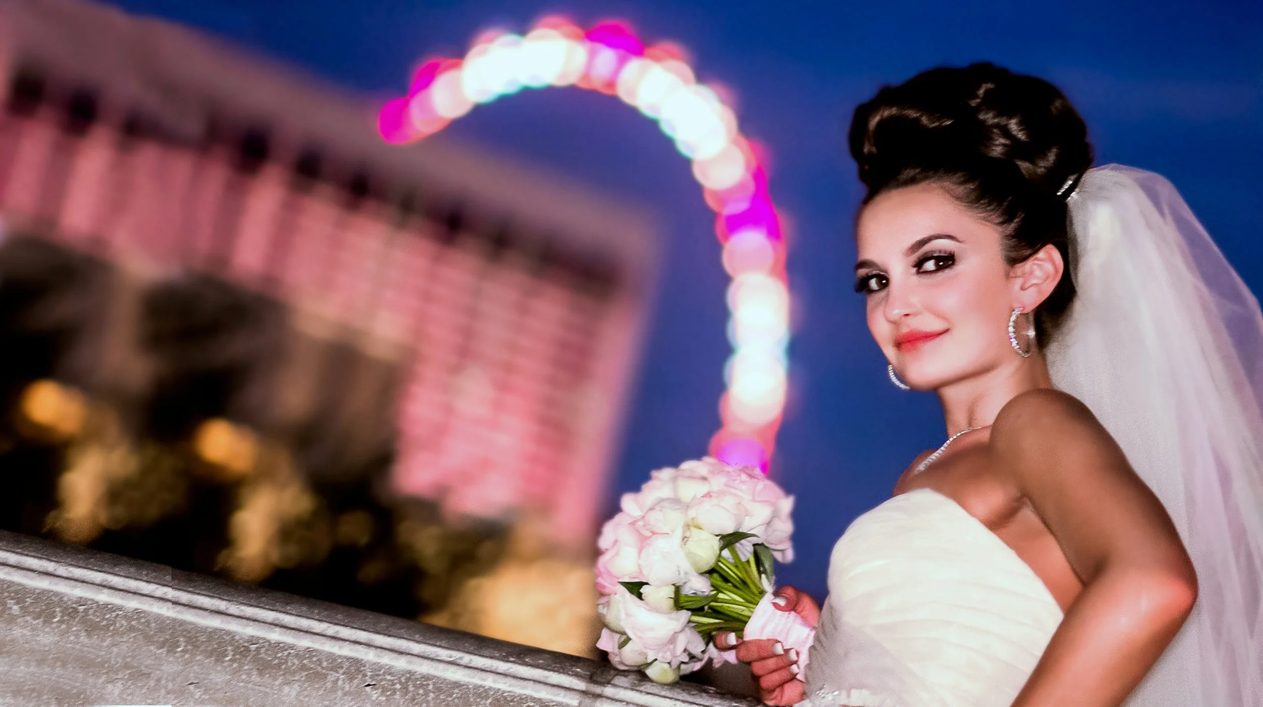 Bride in white wedding dress holding a bouquet of pink roses, with a blurred background featuring colorful city lights and a ferris wheel at night.