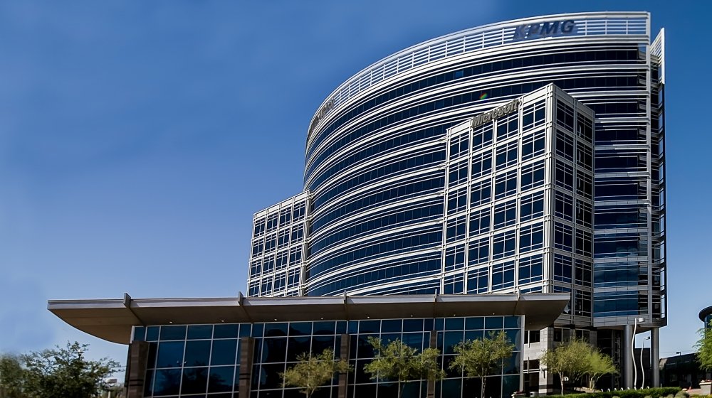 Tall modern office building with glass windows and metal framework, with a blue sky background.