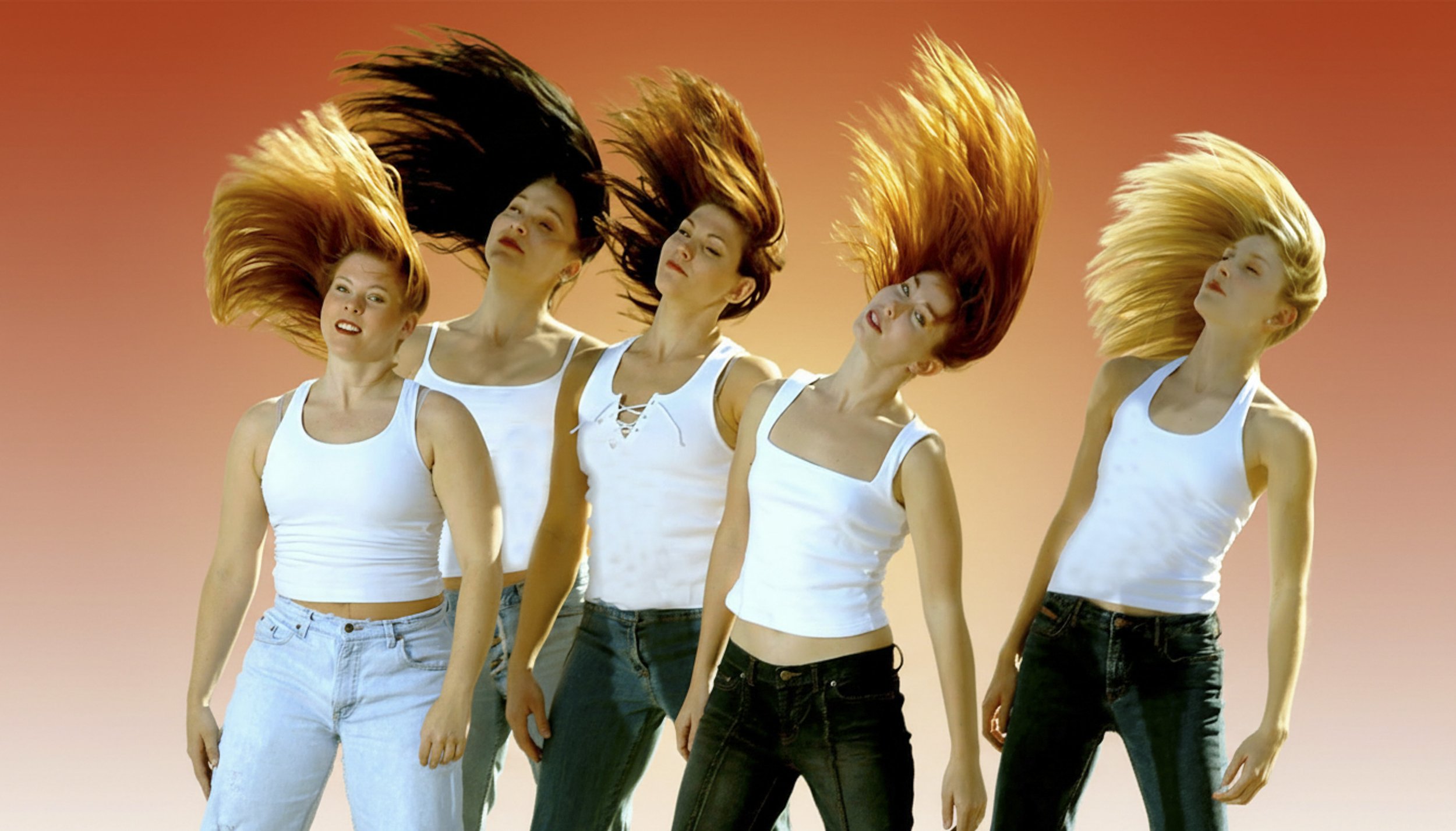 Five women with colorful hair flipping in the air against a sunset sky, wearing white tank tops and jeans.