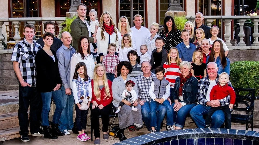 A large family group posing outdoors on the steps of a house during the holidays.