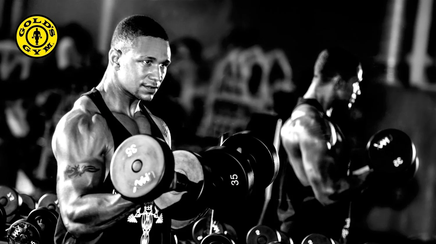 Two muscular men lifting dumbbells in a gym, black and white photo, Gold's Gym logo in the top left corner.