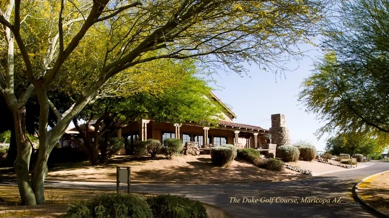 View of the Duke Golf Course clubhouse in Maricopa, Arizona, surrounded by trees and landscaping.