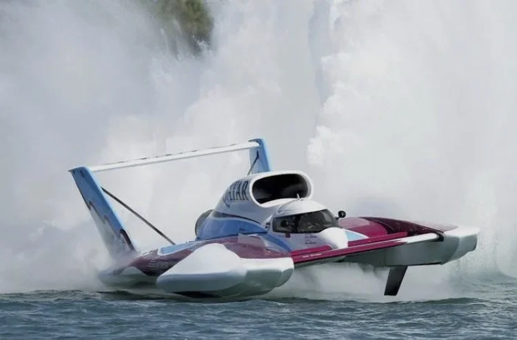 Photo of a hydroplane race boat skimming across the water at high speed, creating a large splash.