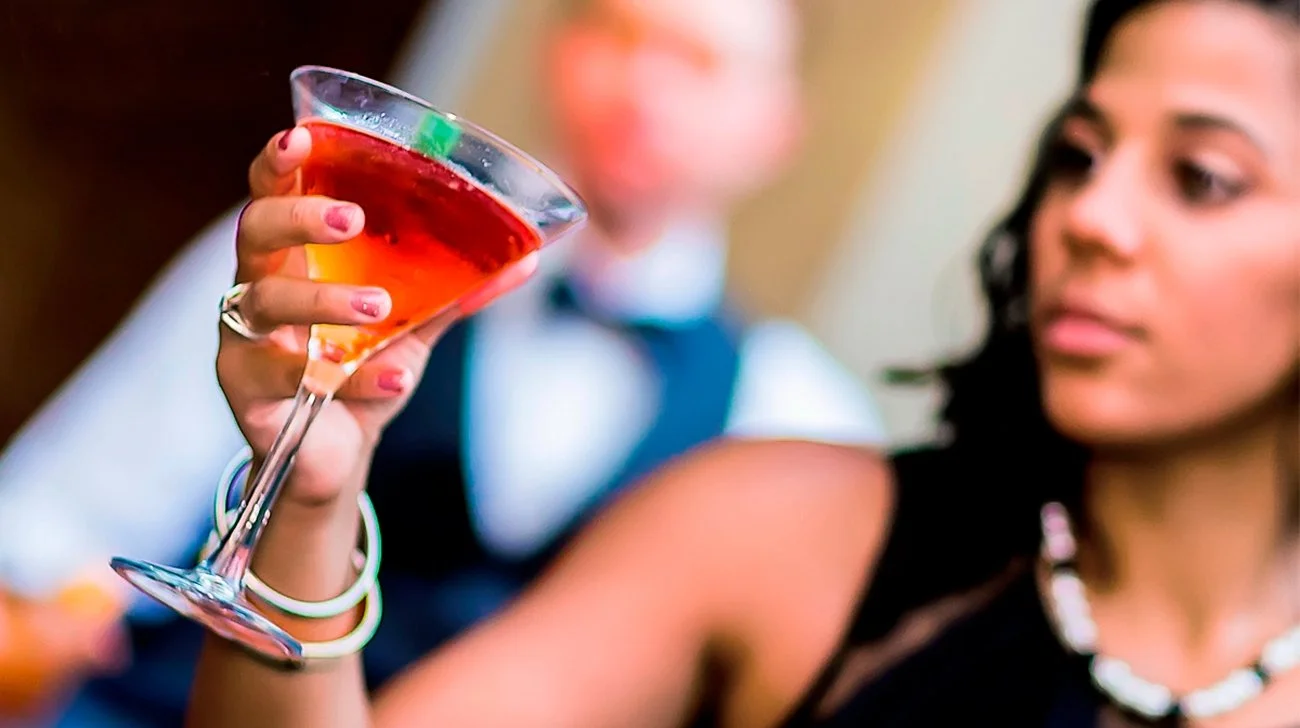 Close-up of a woman holding a cocktail glass with a red drink, another woman in the background blurred