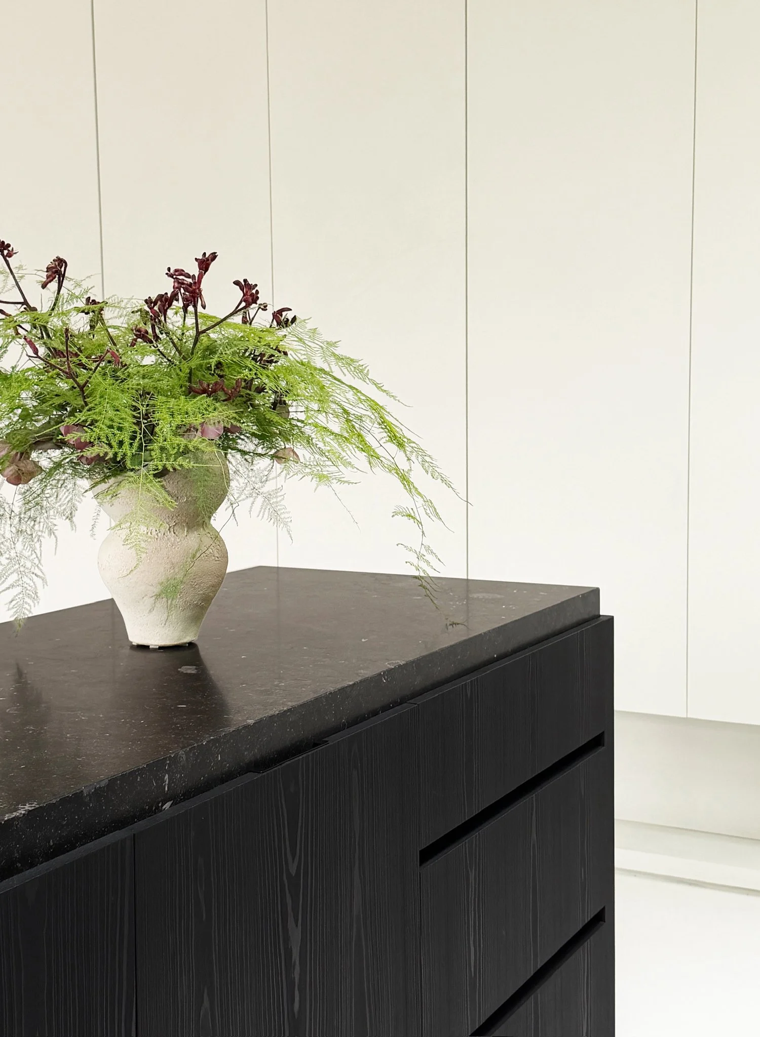 Sculptural plaster vase with a botanical arrangement sitting on a dark stone kitchen island with an ebonized oak base.