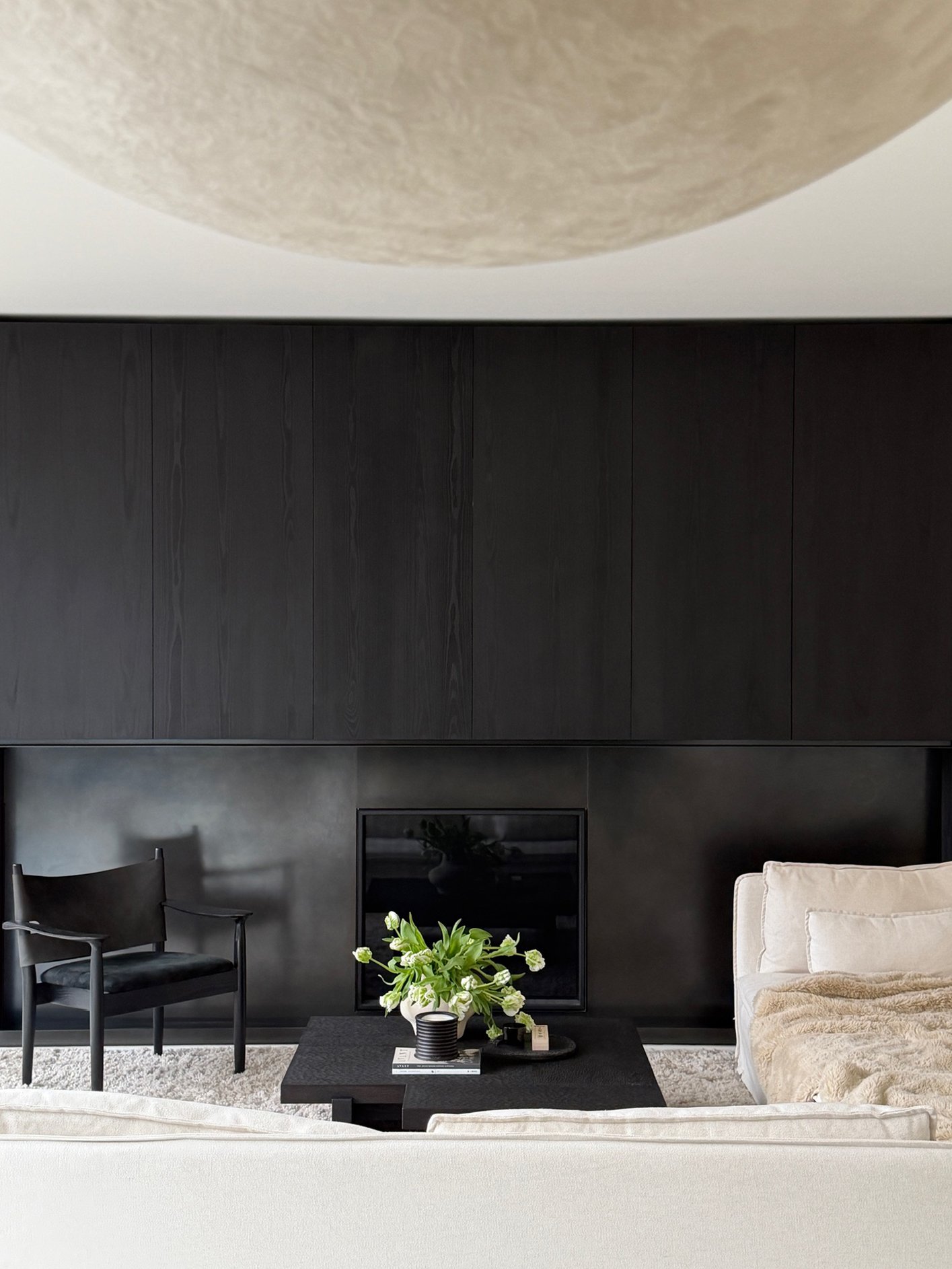Minimalist living room showcasing ebonized oak wall paneling over a raw steel fireplace surround, paired with soft textural seating.