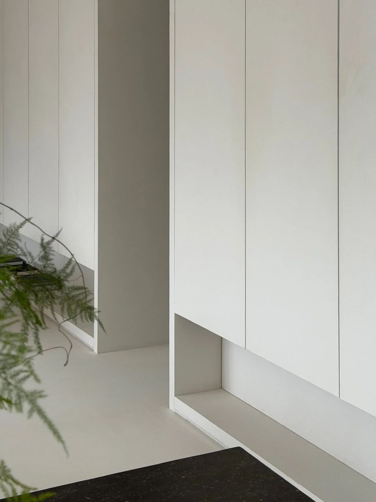 Minimalist hallway storage featuring seamless, plaster-finish closet doors and a recessed open architectural shelf.