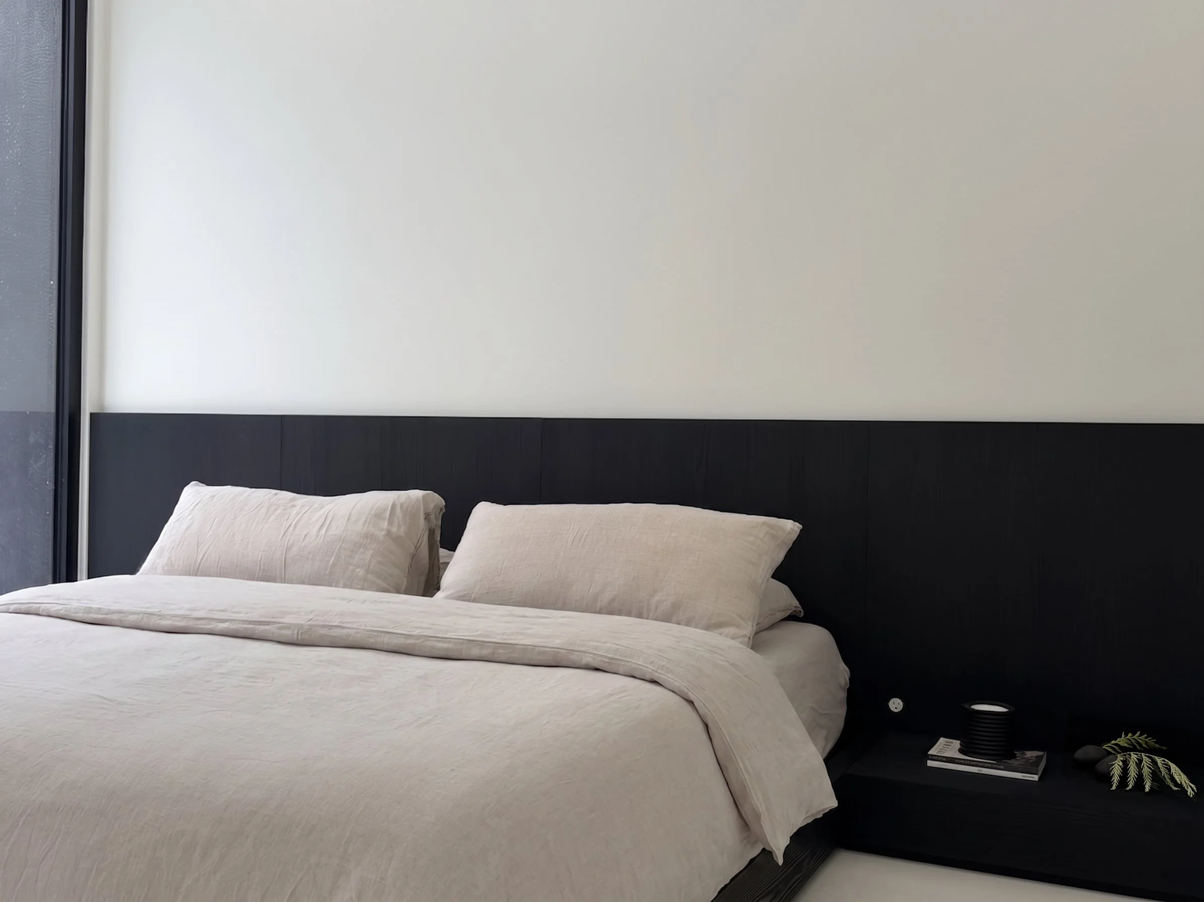 Minimalist bedroom design featuring a continuous low ebonized oak headboard contrasting against smooth, light-colored walls.