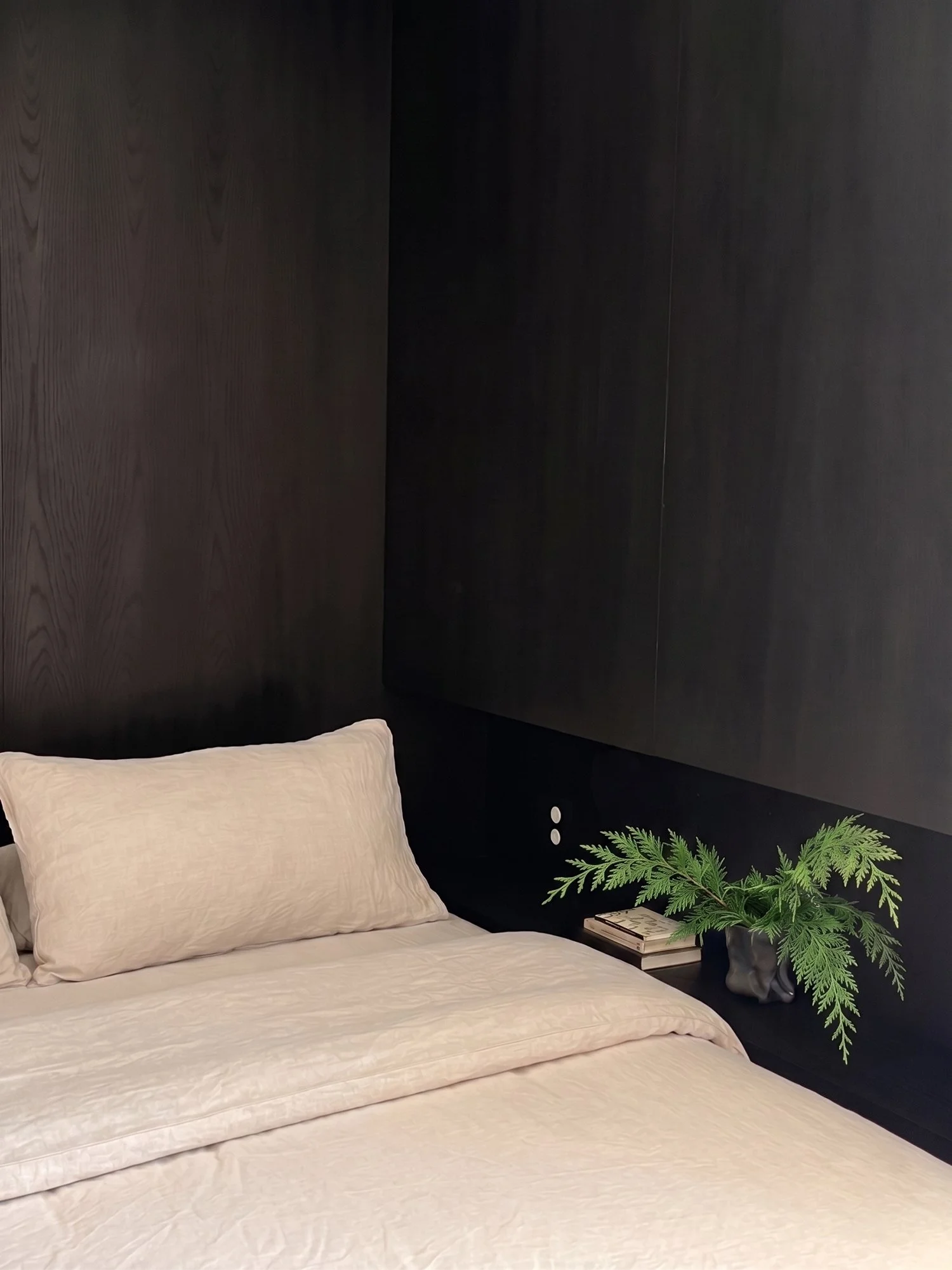 Minimalist bedroom featuring a blackened oak paneled wall, natural linen bedding, and a built-in dark wood nightstand.