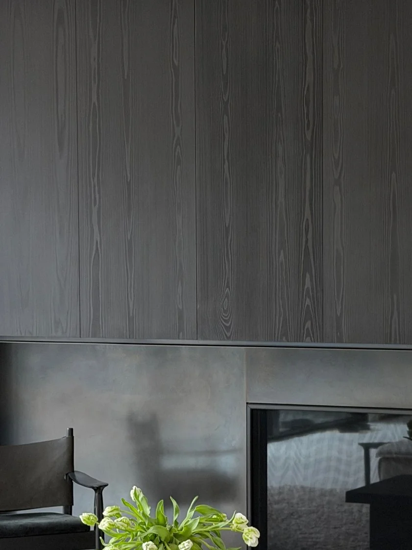 Minimalist living room showcasing ebonized oak wall paneling over a raw steel fireplace surround, paired with soft textural seating.
