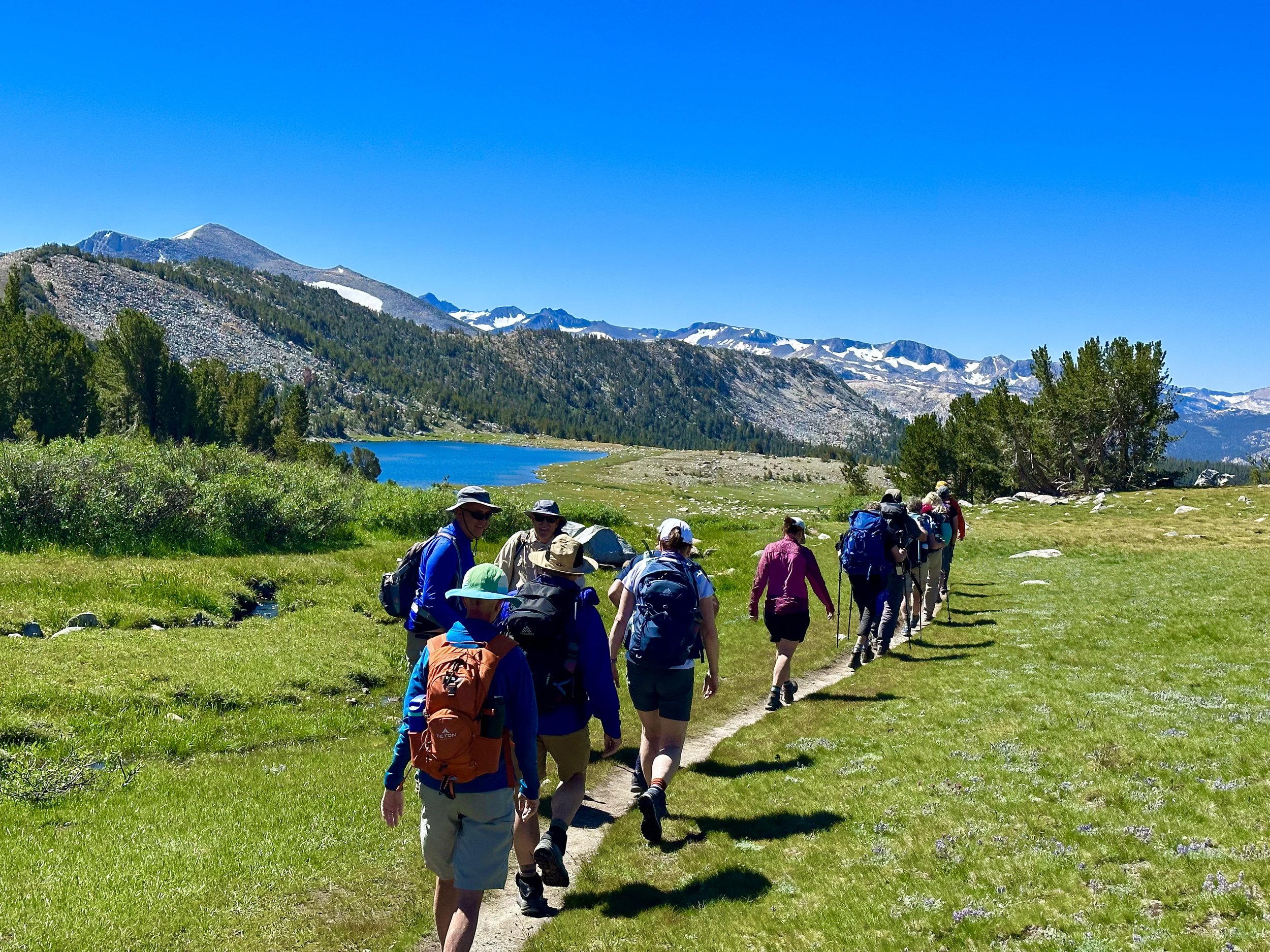 A group of hikers on a high alpine trail near a lake.