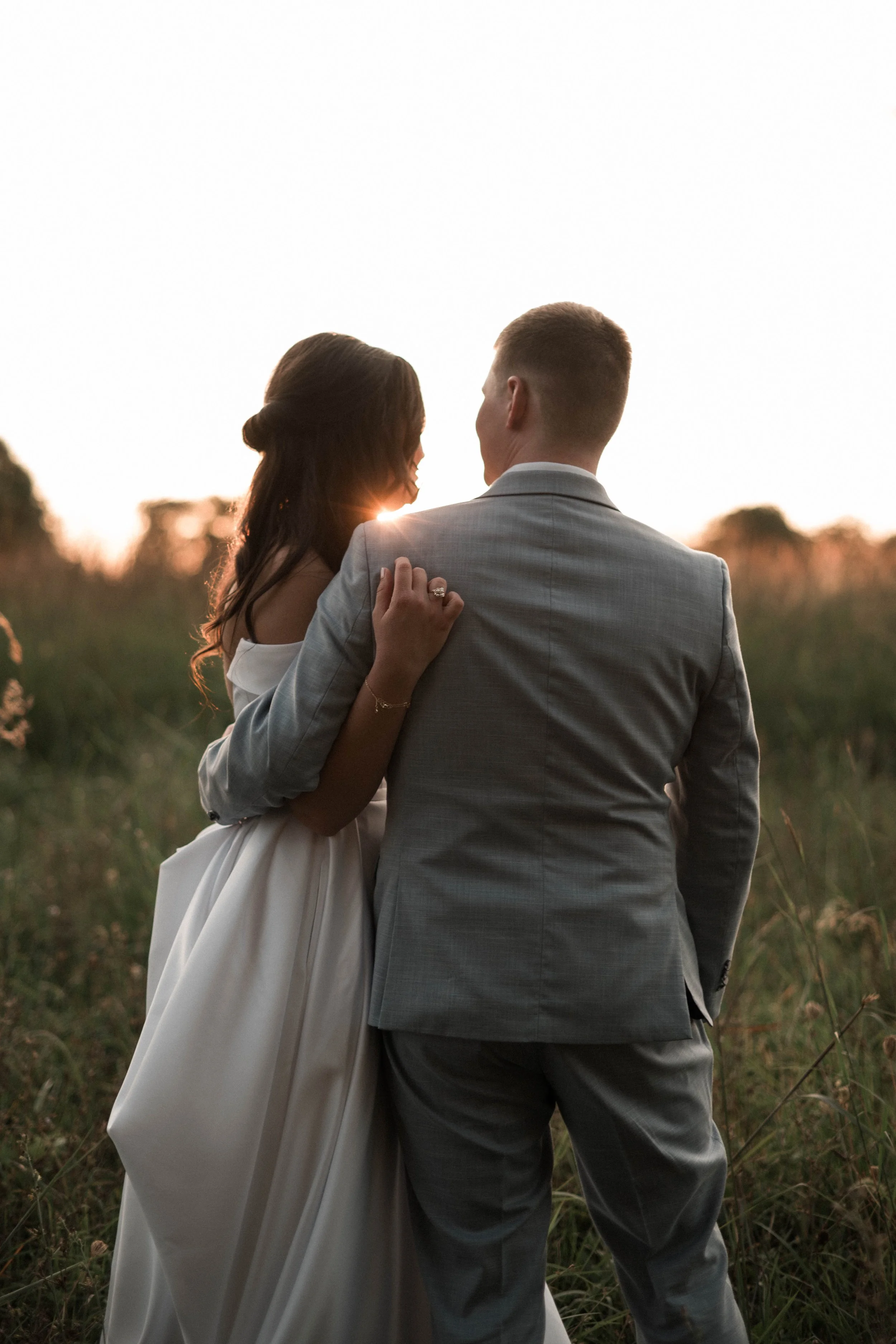 A bride and groom embrace during golden hour in a field after their wedding reception. 