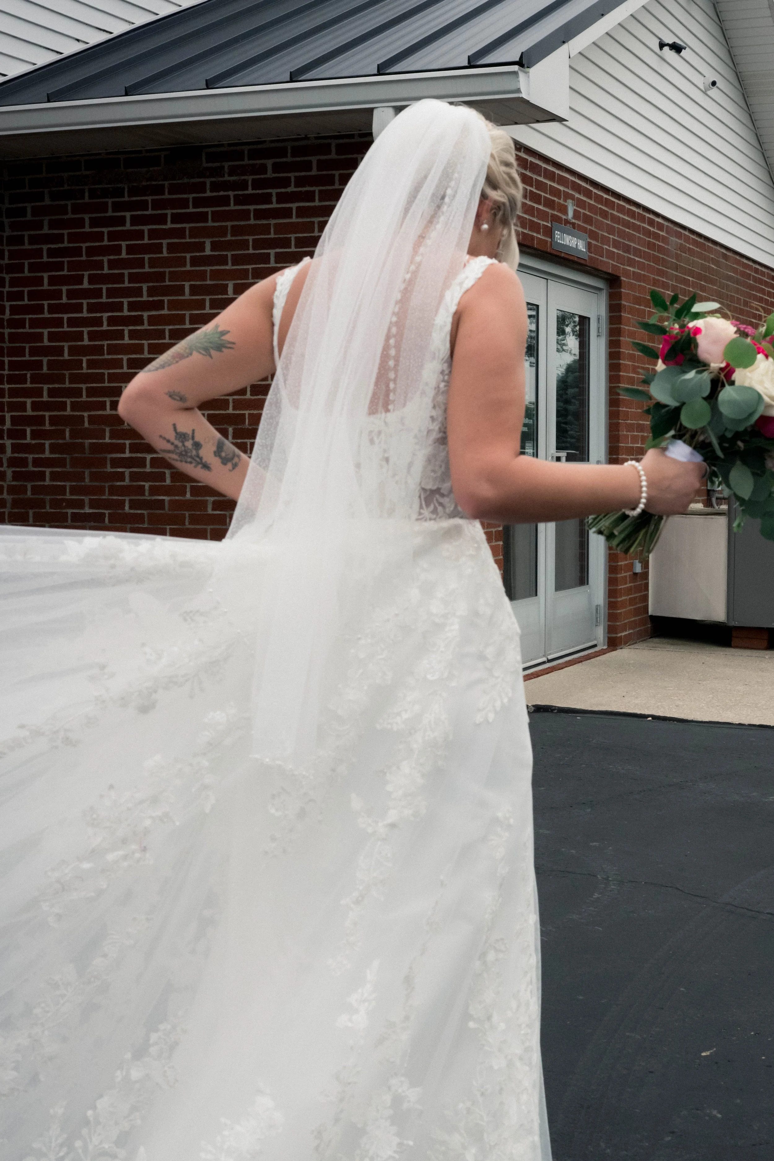 A candid photo of a groom helping a bride carry her wedding dress as she walks. 
