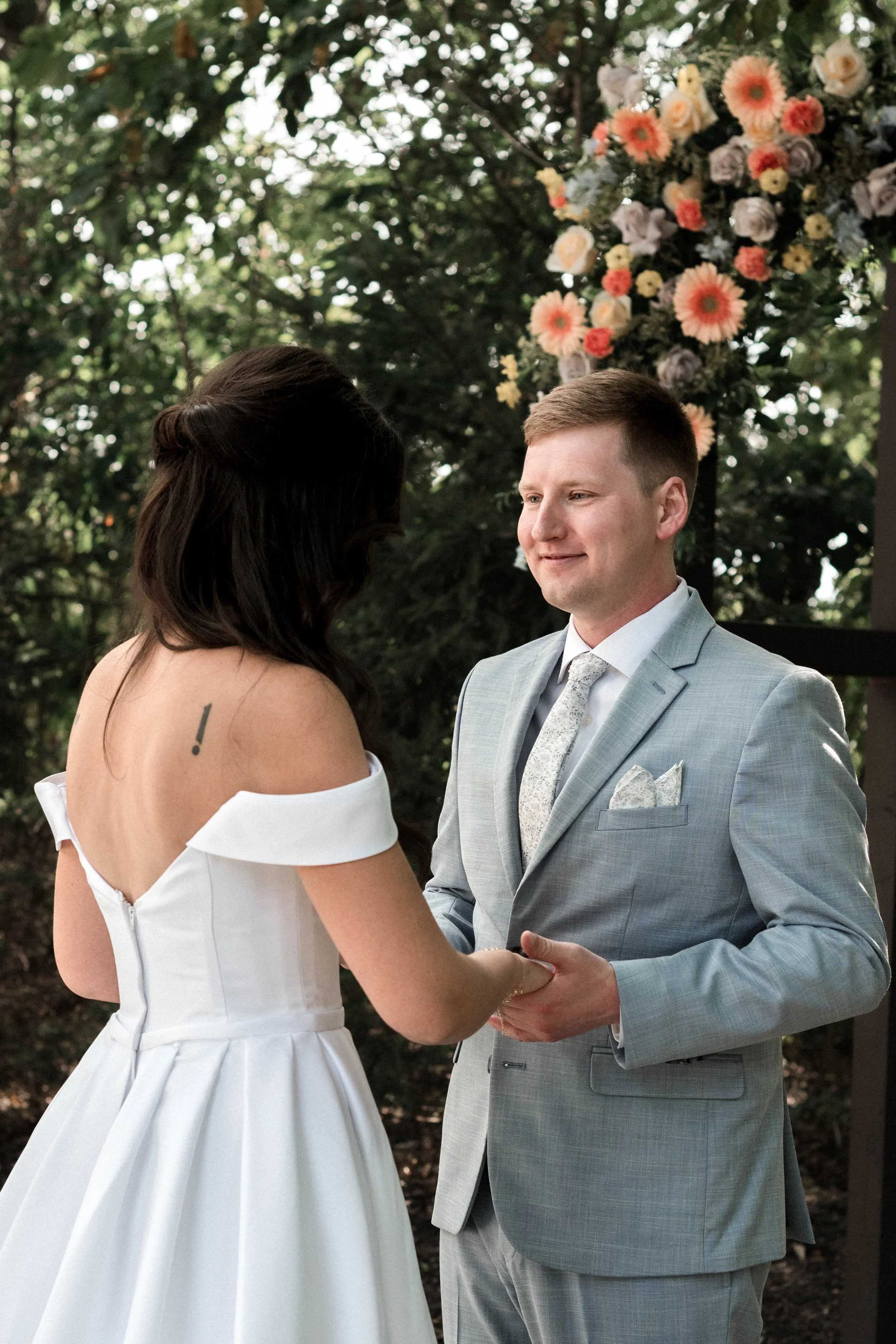 A couple exchanging vows at their outdoor wedding ceremony, with a colorful floral arrangement in the background.