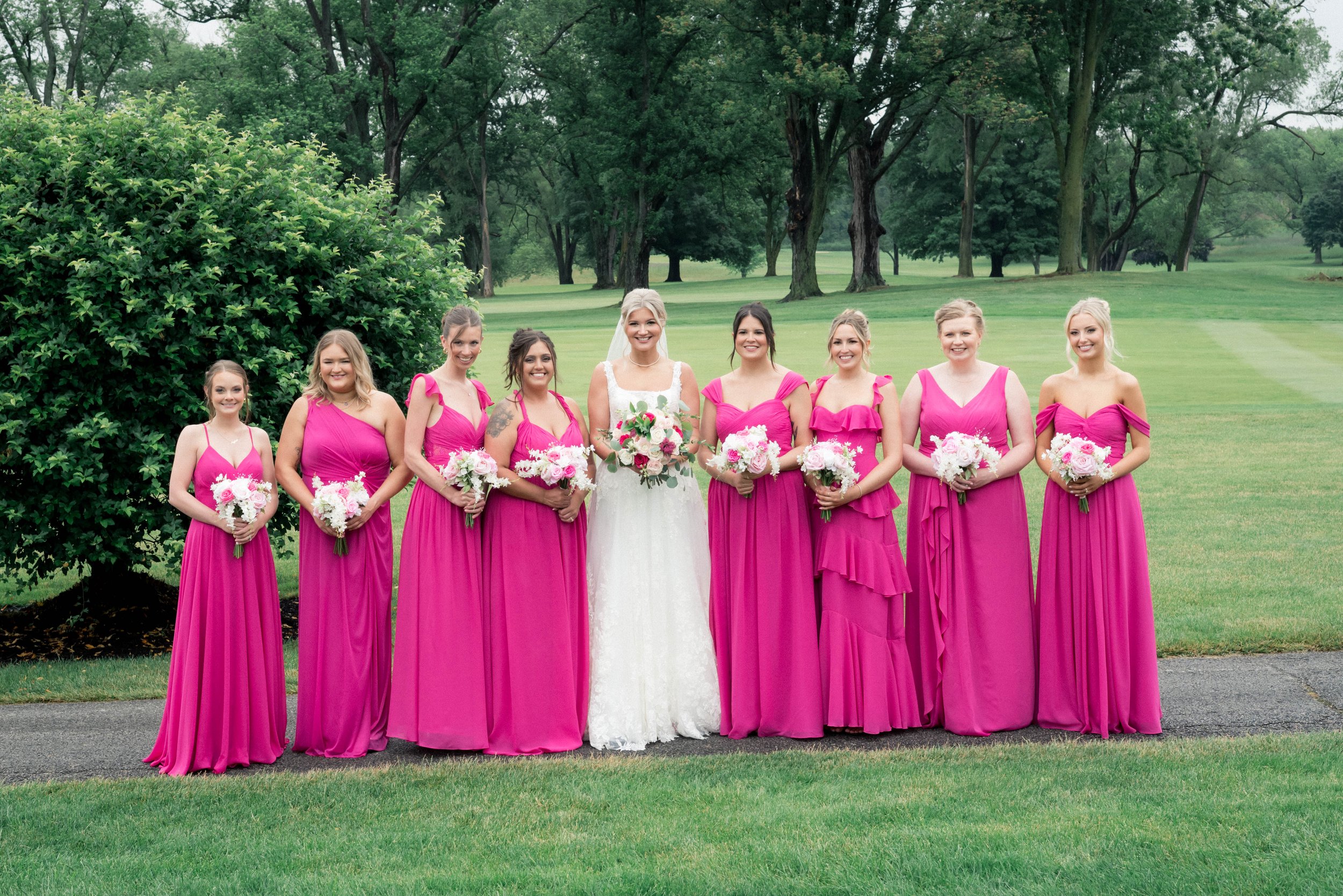 A bride with her bridal party standing at a country club wedding venue. The bride is holding a beautiful bouquet of flowers, as well as her bridesmaids who are in bright pink gowns. They are posing for professional wedding photos in Columbus, OH.