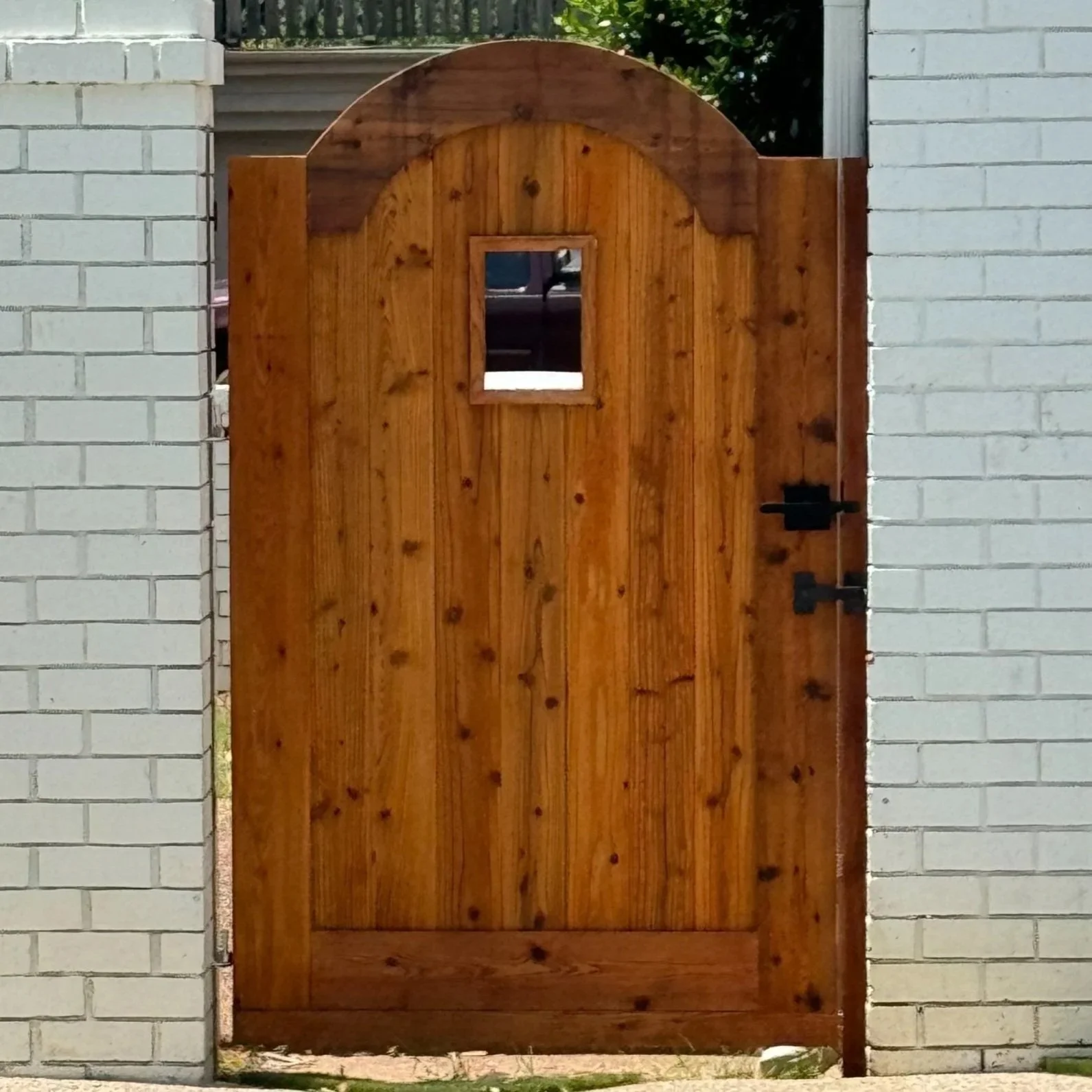 Wooden gate with a small square window, flanked by white brick walls.