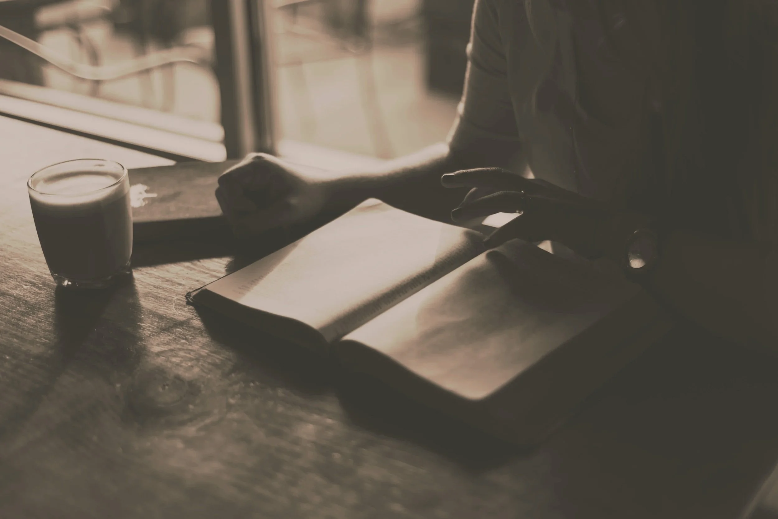 Person working at a wooden table with a coffee mug, an open notebook, and a pen, near a window with sunlight streaming in – Nordica Scientific.