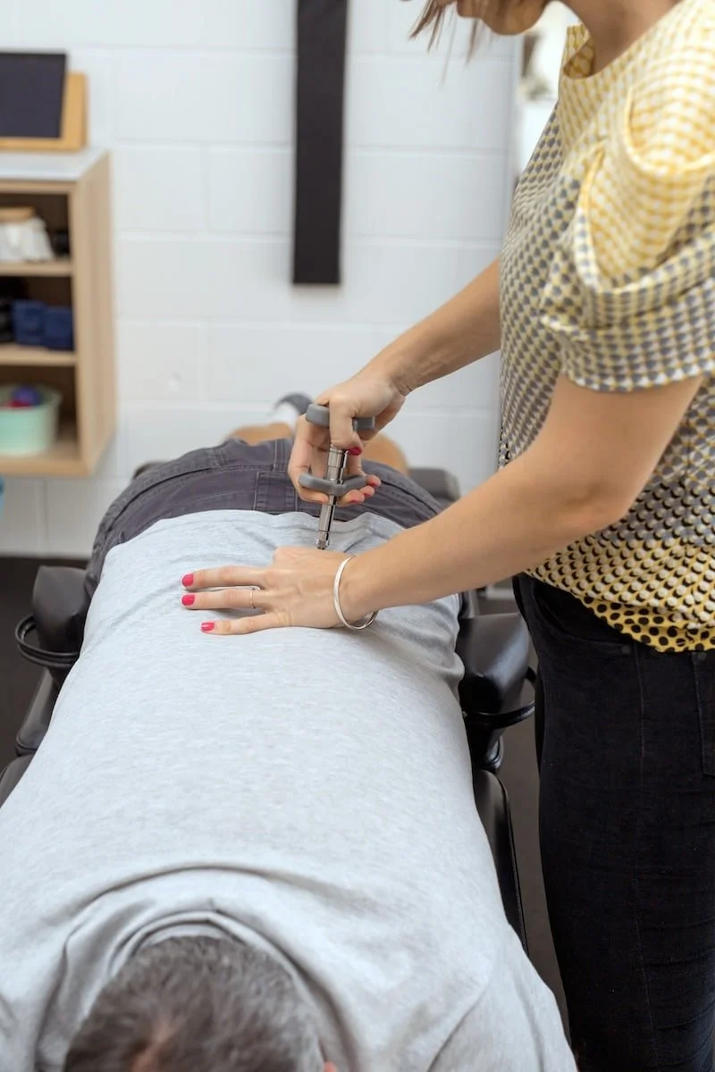 A chiropractor performs an adjustment on a patient lying face down on a chiropractic table.