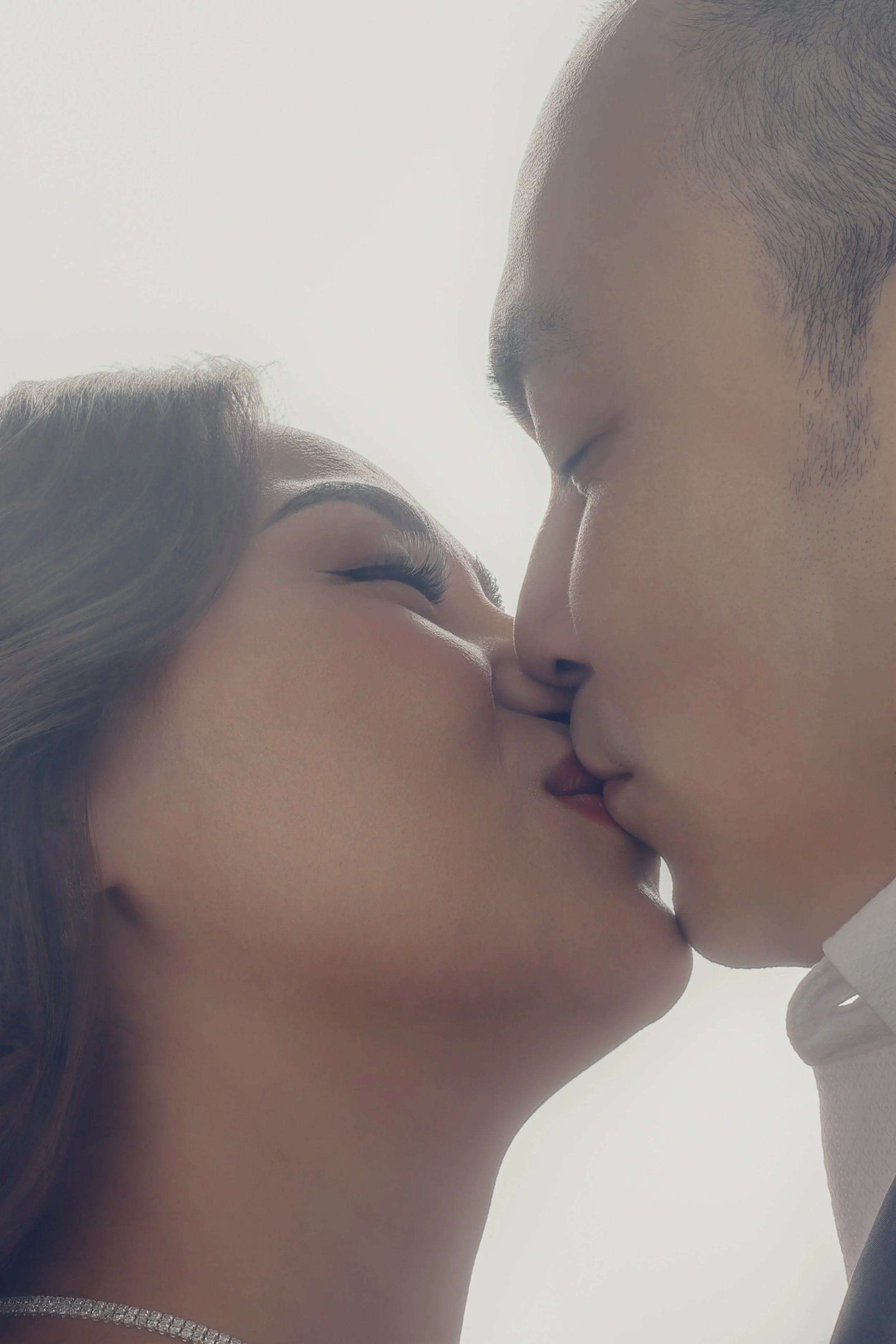A couple kissing with eyes closed, close-up view, backlit